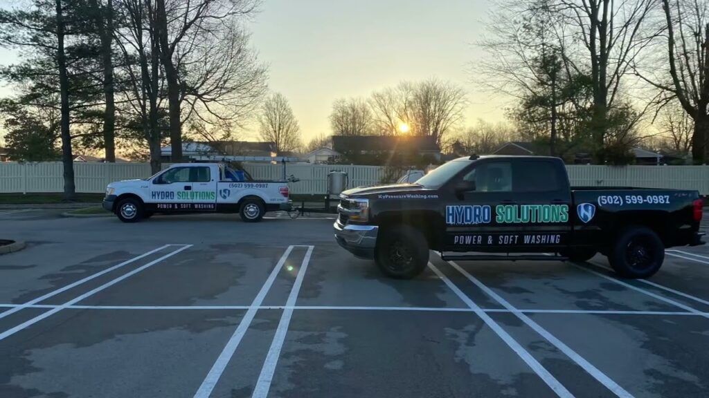 Two Hydro Solutions pressure washing trucks parked in a parking lot with a sunset in the background.