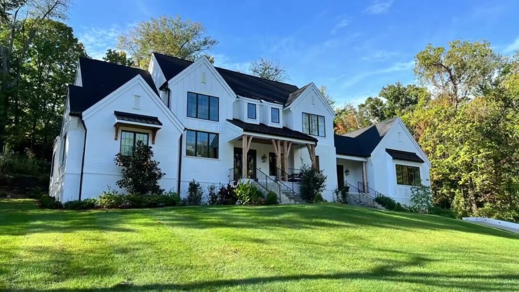 Modern white house with lush green lawn and surrounding trees.
