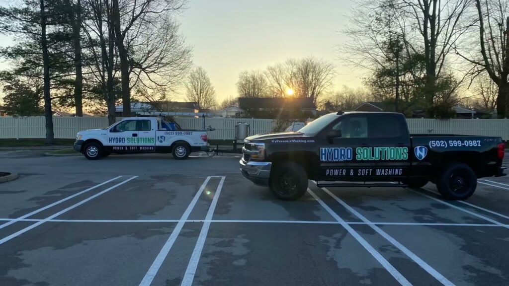 Two Hydro Solutions pressure washing trucks parked in a parking lot with a sunset in the background.